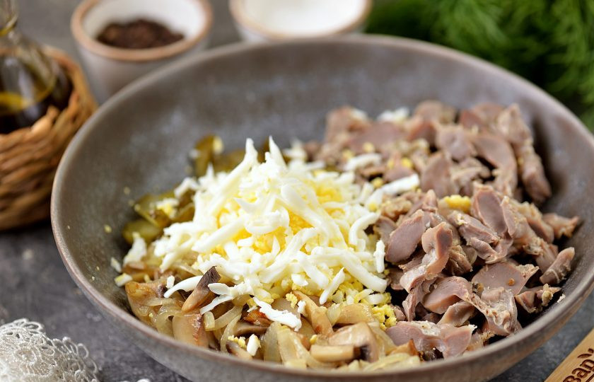 1. Этап. Бюджетный салат с куриными желудками и жареными грибами: Огурец и вареное яйцо нарежьте соломкой, добавьте в миску.
