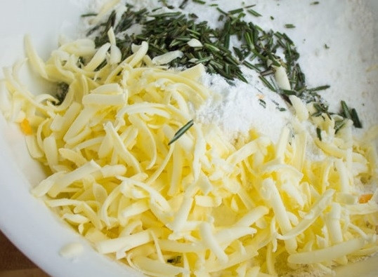 1. Этап. Сырное печенье с клюквой и розмарином: 1. В глубокой мисочке соедините просеянную муку, разрыхлитель, соль и сахар. Перемешайте и добавьте замороженное сливочное масло, тертое на терке. Добавьте щепотку розмарина и перемешайте.