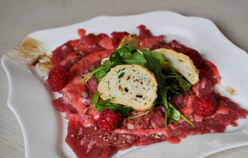 1. Этап. Карпаччо из говяжьей вырезки: Возьмите большое блюдо, на которые вы будете выкладывать карпаччо. Смажьте его дно бальзамическим кремом. Выложите на тарелочку мясо, полейте соусом. Затем выложите на кусочки говядины немного малины, рукколу и соус 