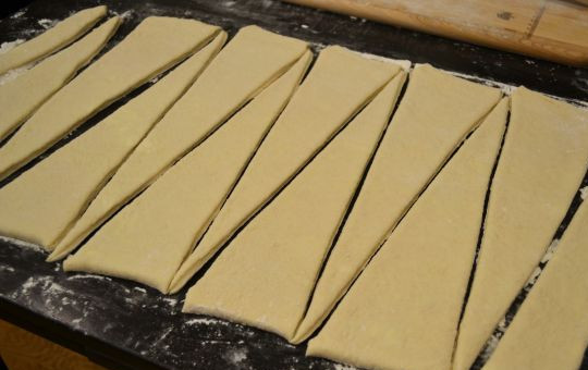 1. Этап. Круассаны из слоеного бездрожжевого теста: 1. Тесто нужно разморозить и раскатать слегка. Затем с помощью острого ножа нарезать длинными треугольниками. Чтобы было проще работать с тестом, рабочую поверхность можно можно присыпать мукой.