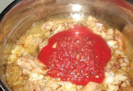 1. Этап. Грудинка свиная тушеная: Добавляем лук к мясу. Выливаем бульон. Добавляем томатную пасту и аджику. Доводим всё до кипения. Потом тушим 40 мин. под крышкой на медленном огне.