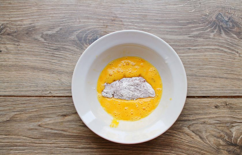 1. Этап. Куриные нагетсы в кукурузной панировке в духовке: Яйцо разбейте в миску и перемешайте вилкой до однородности. Опустите в яйцо каждый кусочек курицы в муке, чтобы они полностью покрылись.