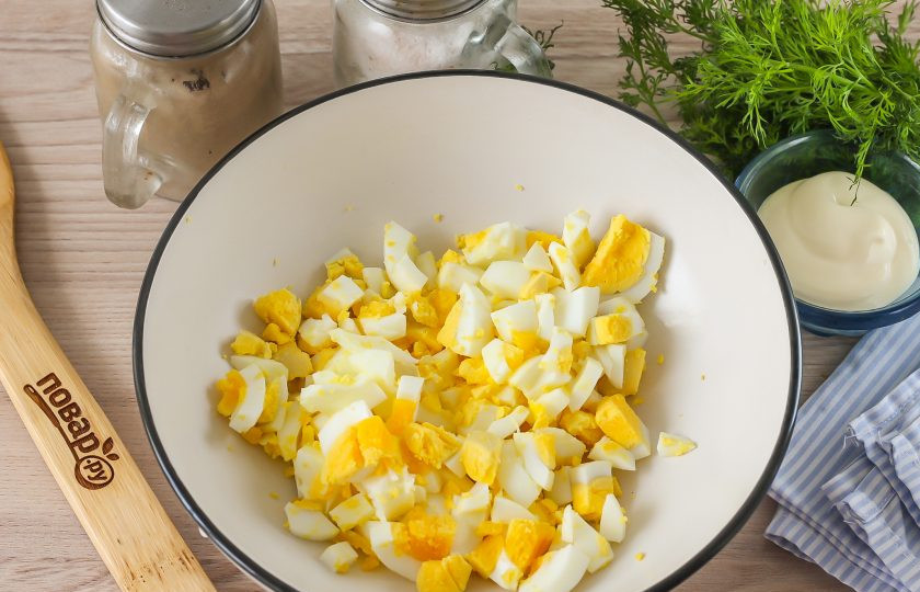 1. Этап. Салат с консервированной горбушей и яйцами: Куриные яйца нарежьте мелкими кубиками с помощью специального девайса или ножа, высыпьте нарезку в глубокую емкость.
