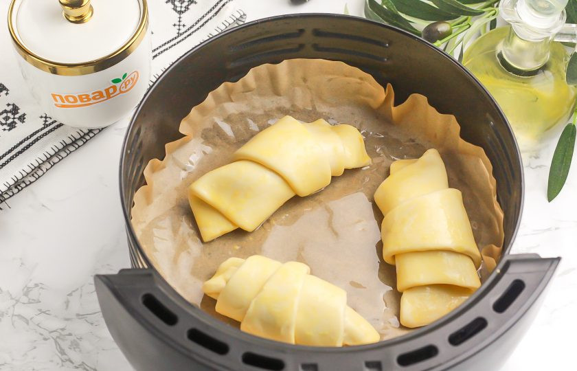 1. Этап. Круассаны в аэрогриле: Выложите в чашу аэрогриля пергаментную бумагу и смажьте ее растительным маслом. Выложите на бумагу круассаны на равном расстоянии друг от друга, так как они увеличатся при выпекании.