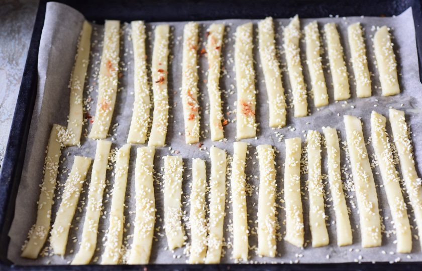 1. Этап. Хрустящие солeные палочки к пиву: Все нарезанные ленты теста выложите на противень застеленный пергаментом для выпекания. Заготовки из теста смажьте силиконовой кистью взболтанным яйцом или теплой водой и присыпьте обильно кунжутом.