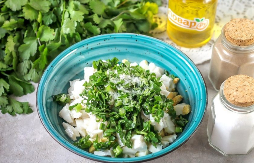 1. Этап. Салат с кальмарами и кинзой: Промойте кинзу и зеленый лук, измельчите и добавьте в емкость. Всыпьте соль и молотый черный перец. По желанию можно добавить пару щепоток молотого сушеного чеснока.