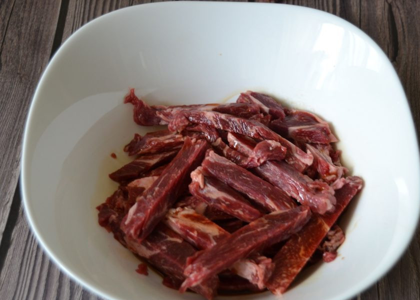 1. Этап. Мясо верёвочкой по-китайски: Нарежьте слегка подмороженное мясо длинными полосками вдоль волокон. Замаринуйте на 20-30 минут в соевом соусе.
