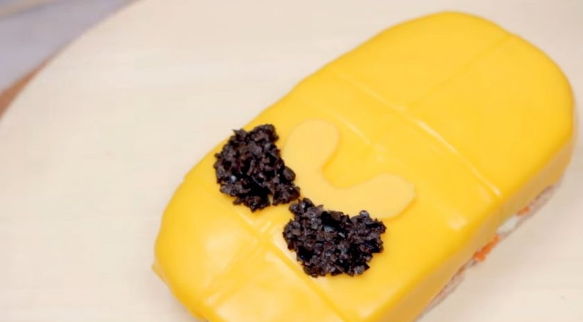 1. Этап. Сэндвич-торт Джейк из Время приключений: 6. Нарисуйте трафарет лица героя и аккуратно вырежьте детали из желтого плавленого сыра: рот и нос. Мелко нарезанные маслины используйте, чтобы аккуратно сформировать глаза Джейка.