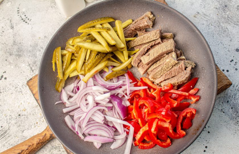 1. Этап. Салат «Садаф»: Красный лук очистите и нарежьте тонкими перьями. Болгарский перец очистите от семян, мякоть нарежьте тонкими полосками. Маринованные огурцы нарежьте тонкой соломкой. Остывшую говядину нарежьте тонкими полосками. Выложите все нарезанные ингредиенты в салатник.