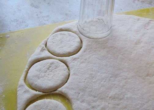 1. Этап. Тесто для вареников на пару на кефире: Готовое тесто достаньте из миски, припылите мукой рабочую поверхность. Раскатайте тесто в пласт толщиной в пять миллиметров при помощи скалки. Вырежете из него кружочки стаканчиком или чашкой.