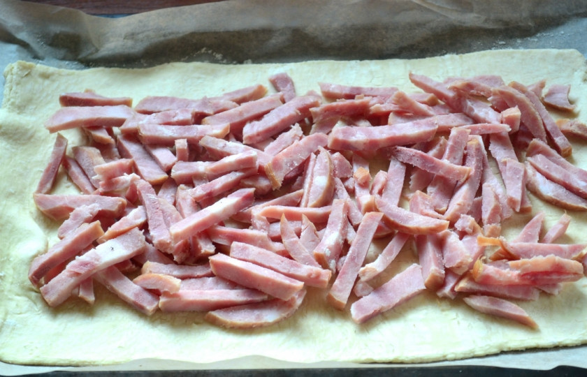 1. Этап. Пирог с начинкой из сыра и ветчины: Переложите раскатанное тесто на противень, застеленный пергаментом, сверху выложите сначала измельченную ветчину.