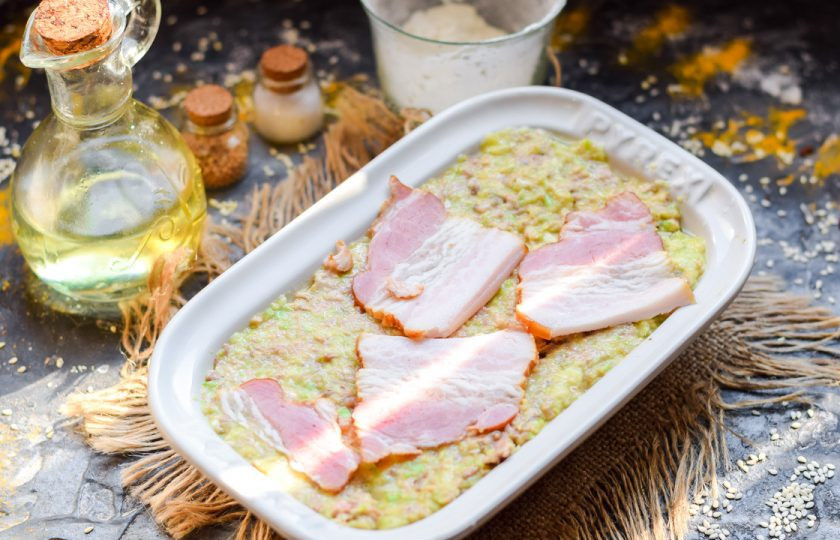 1. Этап. Запеканка из кабачков с фаршем и помидором: Форму для духовки смажьте маслом, выложите подготовленную массу. Поверх выложите немного бекона.