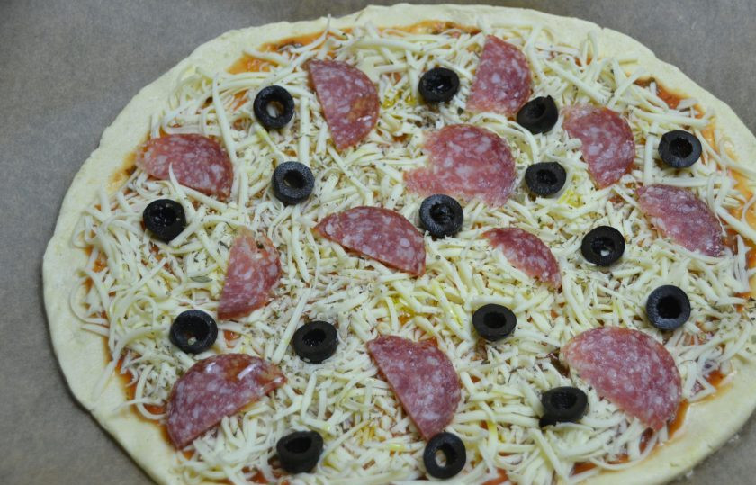 1. Этап. Безглютеновое тесто для пиццы: Сформируйте из теста основу для пиццы, выложите на лист для выпечки. Тесто ведет себя не как обычное тесто из пшеничной муки, оно слегка рассыпается в руках, но работать с ним вполне можно. Смажьте основу для пиццы томатом, выложите тертую на крупной терке моцареллу, ломтики колбасы, маслины, посыпьте сухим базиликом, сбрызните оливковым маслом.