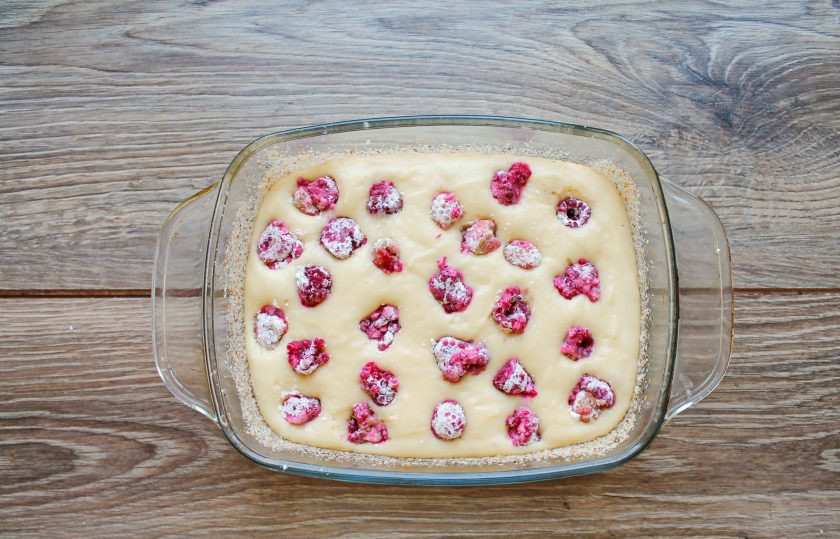 1. Этап. Пирог с малиной на кислом молоке: Форму для запекания размером 16*21 сантиметр смажьте растительным маслом и вылейте тесто, разровняйте. Сверху разложите малину, смешанную с крахмалом, и утопите немного в тесто.