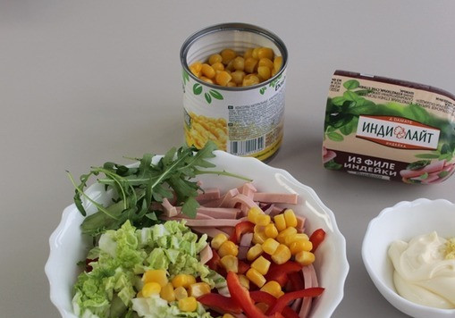 1. Этап. Салат с пекинской капустой и колбасой: В чашке соедините все ингредиенты, добавьте кукурузу и нарезанную зелень, желательно петрушку, я добавила рукколу. Заправьте салат майонезом, который смешайте с выдавленным зубчиком чеснока. Перемешайте салат.