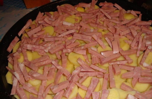 1. Этап. Картофельная запеканка с ветчиной: 4. На картофель выложите кусочки ветчины. Ветчину покройте слоем лука. В качестве следующего слоя используйте натертый на крупную терку сыр.