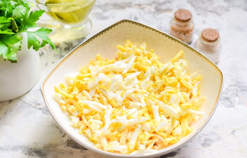 1. Этап. Салат Чикаго с копченой грудкой: Куриное яйцо сварите вкрутую, почистите и натрите на средней терке. Выложите яйцо поверх сыра.