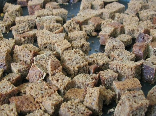 1. Этап. Бородинский квас без дрожжей: 2. Подготовьте противень и застелите его пергаментом. Выложите кубики хлеба и отправьте в разогретую духовку. Подсушите немного, постоянно помешивая. Основную часть выложите в мисочку и оставьте несколько, чтобы немного хорошо поджарились. Использование в рецепт приготовления бородинского кваса без дрожжей пережаренных сухарей дает более насыщенный цвет и вкус.