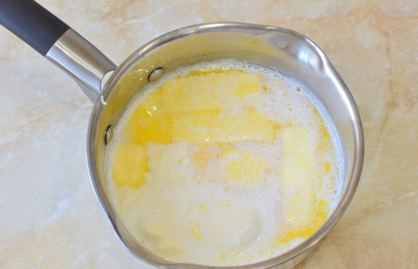 1. Этап. Торт с консервированными персиками и взбитыми сливками: В ковш налейте молоко и добавьте к нему сливочное масло. Поставьте на огонь и доведите до кипения. Проварите, чтобы масло полностью растаяло.