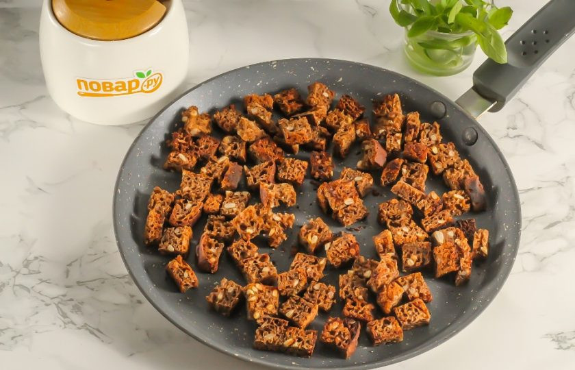 1. Этап. Окрошечный квас с изюмом: Нарежьте черный хлеб кубиками или брусочками. Поджарьте в сухой сковороде примерно 3-4 минуты. Можно зажарить прямо до сильной румяности, чтобы сухарики придали квасу более насыщенный цвет. Остудите их примерно 10 минут.