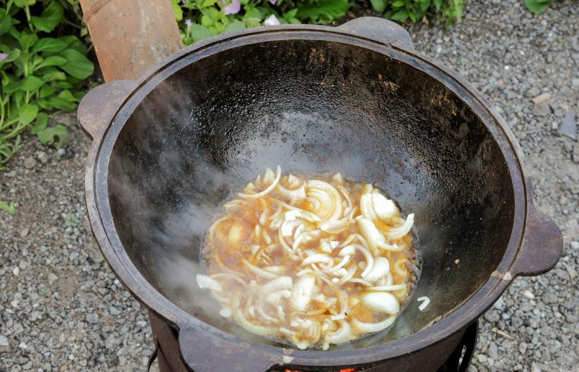 1. Этап. Куриные окорочка в казане на костре: Переложите курицу пока на тарелку, а в казан отправьте нарезанный лук. Если масла осталось от курицы много, можно большую часть слить. Можно добавить соль и молотый перец по вкусу. Не переборщите, не забывайте, что курица уже солёная.