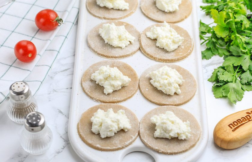 1. Этап. Вареники на гречневой муке: Разделите тесто на несколько частей, теперь оно станет пластичным и будет легко раскатываться. Раскатайте его в округлый пласт и вырежьте стаканом круги, обмакивая стакан в муку. Перемешайте творог с солью и выложите на каждый круг немного начинки. Если любите сладкие вареники, то добавьте в начинку 40-50 грамм сахара.