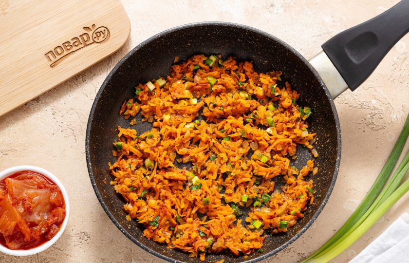 1. Этап. Пельмени с тофу и кимчи: Морковь очистите и натрите на терке, репчатый лук нарежьте на мелкие кубики, а чеснок пропустите через пресс. В сковороде обжарьте овощи с растительным маслом до мягкости и золотистого цвета. В конце добавьте красный перец кочукару, молотый имбирь, мисо-пасту и мелко нарезанный зеленый лук. Прогрейте все вместе еще 1-2 минуты.