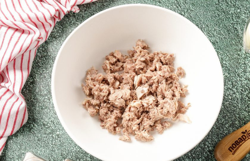 1. Этап. Салат с тунцом, огурцами и кукурузой: Из банки с тунцом слейте масло и разомните его вилкой. У меня была баночка с уже рубленым тунцом, которого я просто откинула на сито. Переложите рыбу в глубокую миску или сразу в салатник.