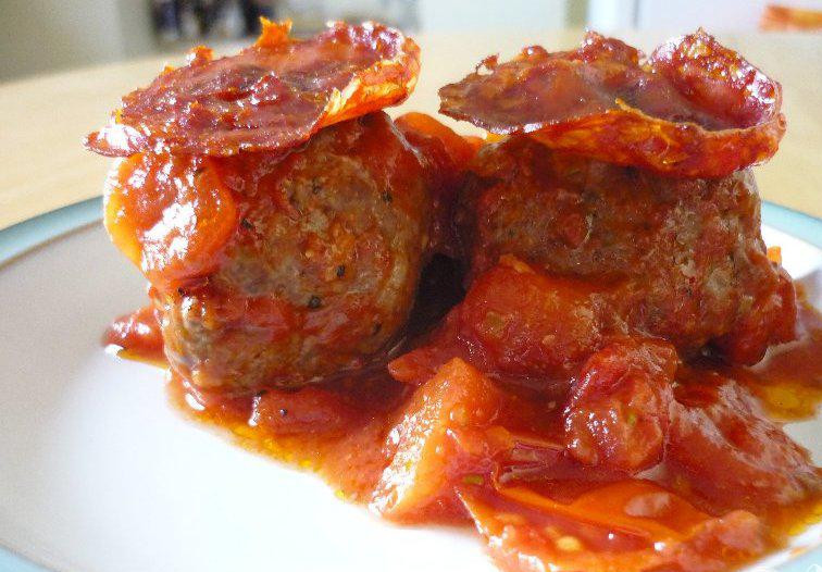 1. Этап. Мясные шарики с чоризо: 3. Пока мясные шарики готовятся, разогреть духовку до 180 градусов. Свиную колбасу чоризо нарезать кружочками, но очень тонко. Выложить колбасу на противень и поставить в духовку на 5 минут. Внимательно следите за колбасой, она может пригореть. Когда мясные шарики будут готовы, выложить их на тарелку и положить кусочек запеченной колбаски на каждый из них. Мясные шарики можно приготовить заранее и разогреть в микроволновке. Чоризо запекать следует прямо перед подачей на стол.