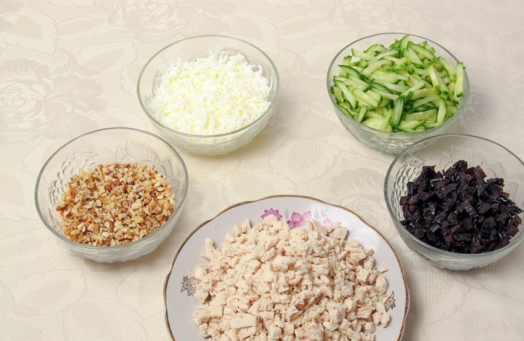 1. Этап. Салат с курицей и грибами слоями: Чернослив замочите в воде на 20 минут, а потом мелко нарежьте. Пару плодов оставьте для украшения. Грудку порубите. Огурец нашинкуйте брусочками. Орехи превратите в крошку, а белки натрите на мелкой тёрке.