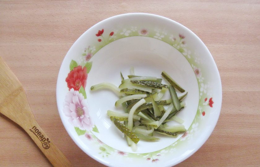 1. Этап. Салат Старорусский с грибами: Соленый огурец нарежьте соломкой и выложите в салатник.