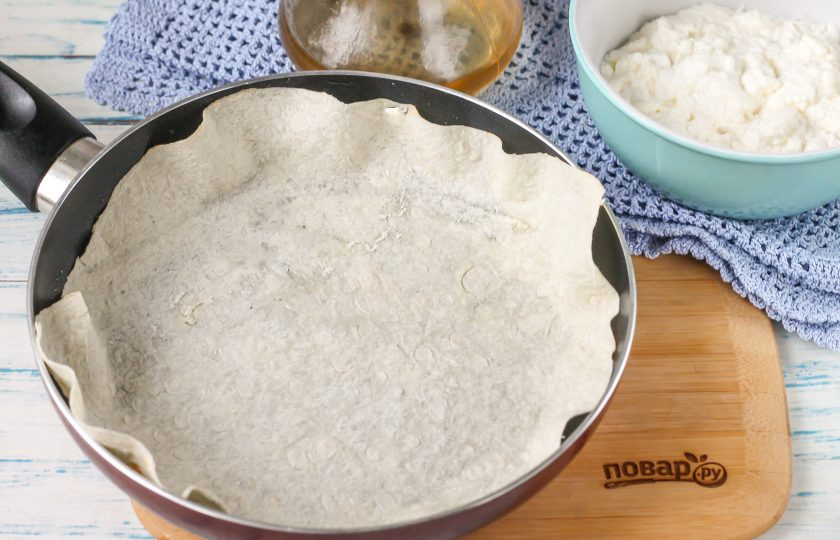 1. Этап. Пирог из лаваша на сковороде: Смажьте сковороду растительным или сливочным маслом, влейте на дно воду, так пирог не подгорит. Вырежьте из лавашей круги по диаметру емкости. Обрезки не удаляйте, их выложите в середину пирога. Поместите на сковороду первый круг лаваша.