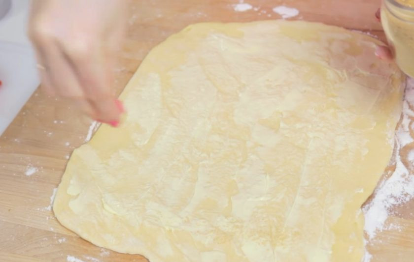 1. Этап. Клубничные улитки: 3. Тесто раскатайте и слегка смажьте сливочным маслом для более сливочного вкуса. Затем посыпьте сахаром и выложите нарезанную небольшими кубиками клубнику.