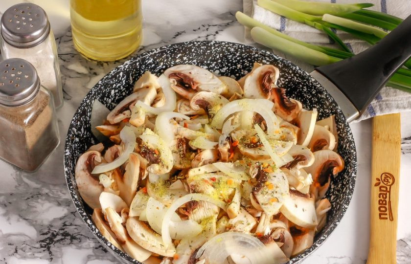 1. Этап. Грибная начинка для блинов: В это время очистите репчатый лук от кожуры и промойте в воде. Нарежьте полукольцами и добавьте в емкость. Посолите и всыпьте овощную или грибную приправу. Аккуратно перемешайте, чтобы соль попала на все грибные ломтики. Благодаря ей они быстрее выпустят жидкость.