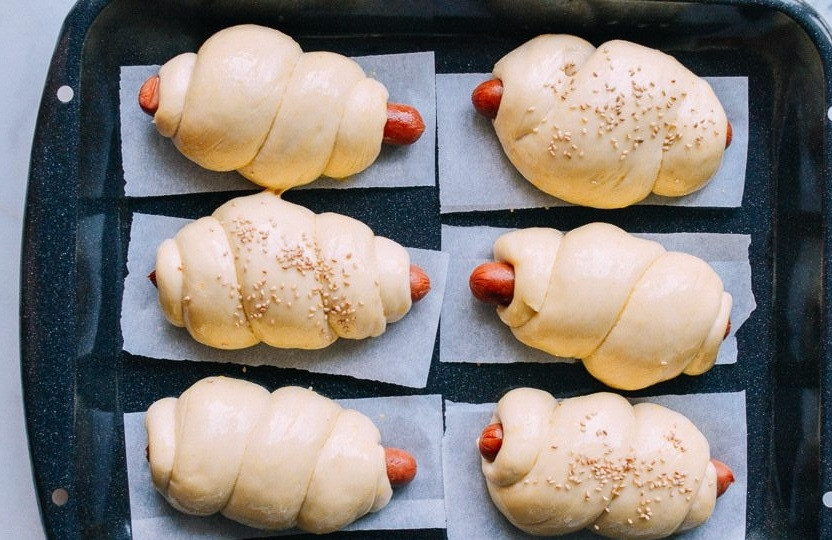 1. Этап. Рецепт сосисок в тесте: 4. Накройте противень полотенцем и оставьте еще на 1 час, за это время выпечка поднимется. Смешайте яйцо со столовой ложкой молока или воды, смажьте им каждую сосиску в тесте. Некоторые сосиски по желанию украсьте семенами кунжута.