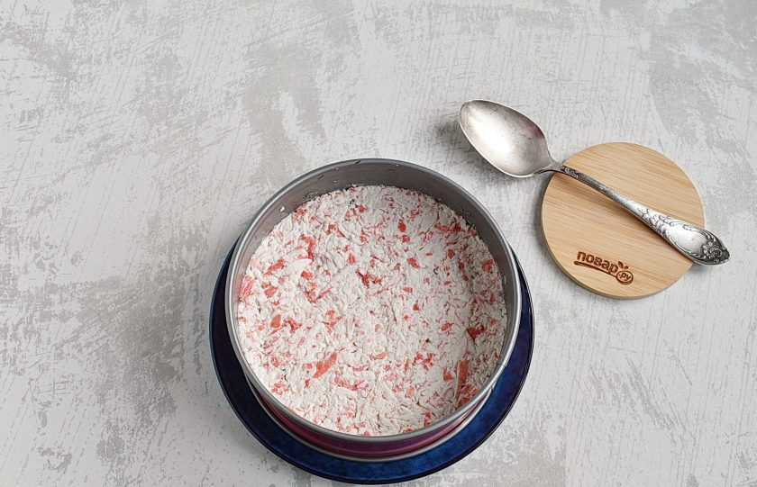 1. Этап. Крабовый салат с рисом и кукурузой: Крабовые палочки натрите на крупной терке и смешайте с майонезом. Количество зависит от сочности палочек. Выложите слой и хорошо уплотните. Накройте форму с салатом пленкой и уберите в холодильник на полчаса для пропитки.