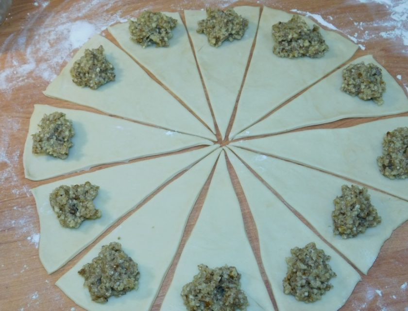 1. Этап. Рогалики с грецкими орехами: Раскатайте тесто и разрежьте на треугольные сектора. Выложите немного начинки на широкую часть.