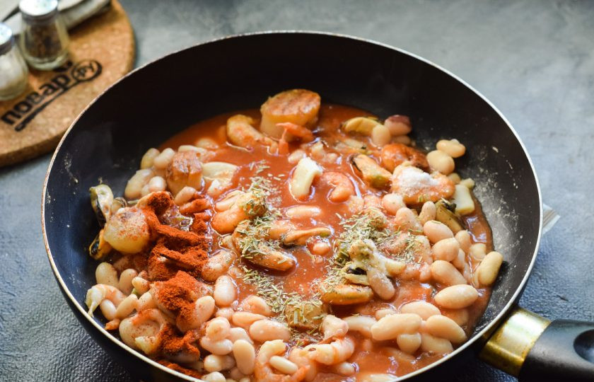 1. Этап. Фасоль с морепродуктами: Томатную пасту разведите в воде, добавьте в сковороду, всыпьте специи.