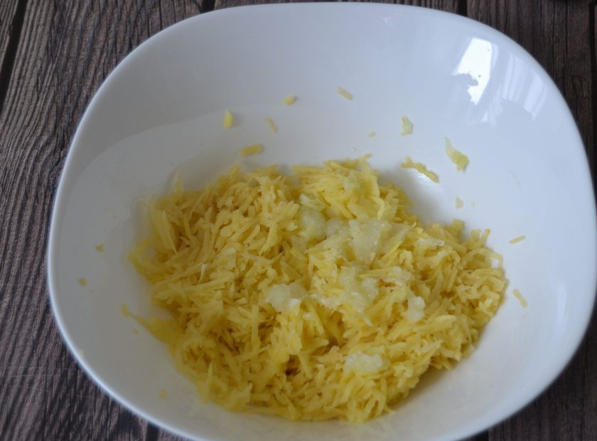 1. Этап. Драники на молоке: В миску натрите картофель, половинку луковицы и зубчик чеснока. Отожмите лишнюю жидкостью.
