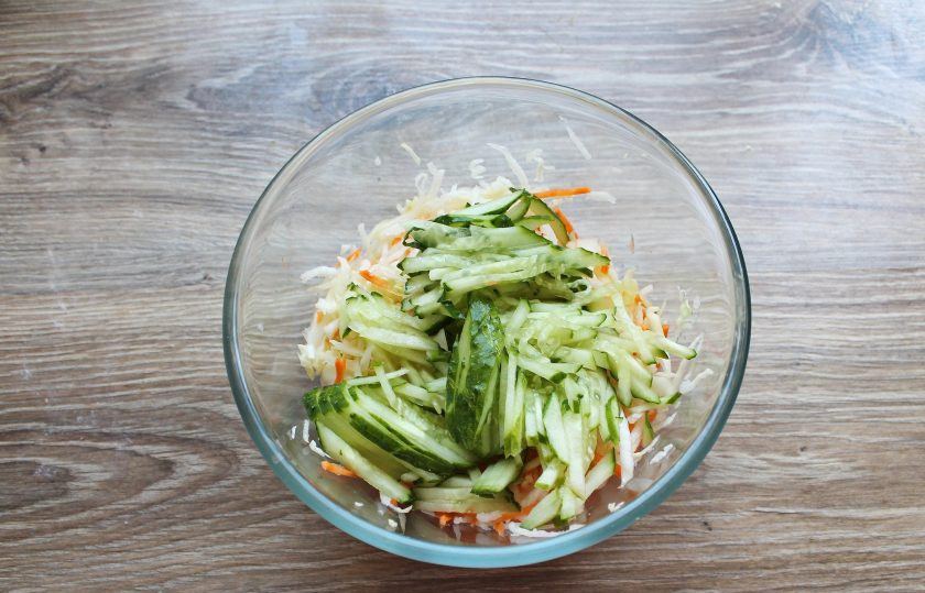 1. Этап. Салат с капустой и дайконом: Огурец порежьте соломкой и выложите в миску с овощами, перемешайте.