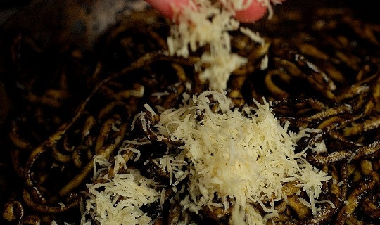 1. Этап. Паста с каракатицей: 7. Натрите на терке сыр, добавьте его на сковороду. Выложите туда же макароны. Аккуратно все перемешайте и снимите с огня.