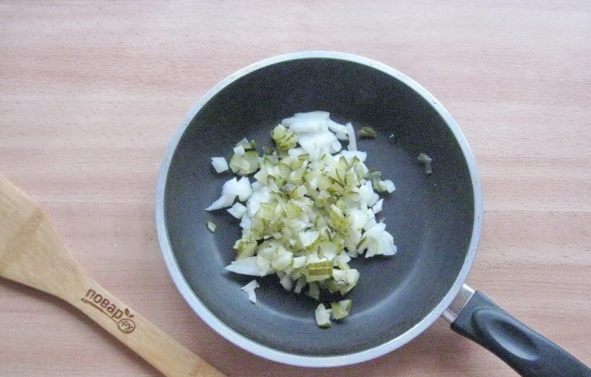 1. Этап. Солянка из судака: Репчатый лук очистите и помойте. Мелко нарежьте лук и соленый огурец. Выложите в сковороду.