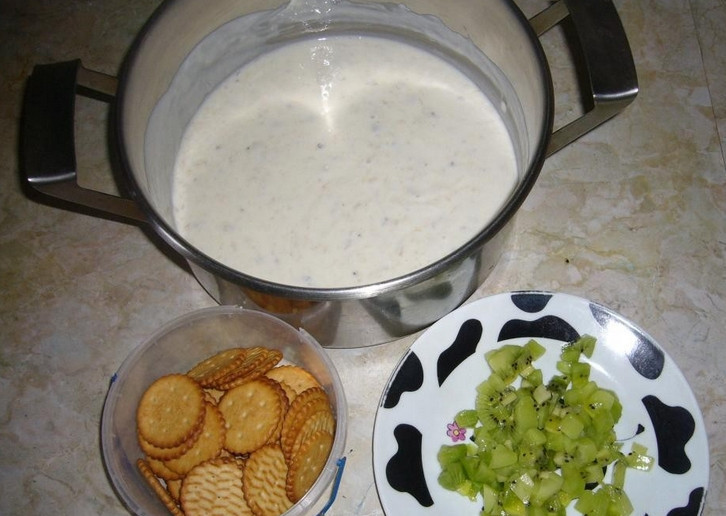 1. Этап. Торт без выпечки из печенья и сметаны: Вливаем в кастрюлю сметану. Добавляем 3 ст.л. сахара, перемешиваем. Банан и киви очищаем, нарезаем небольшими кусочками. Крекер нужно размять скалкой в крошку.