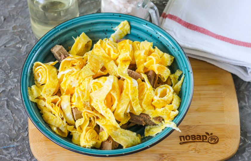 1. Этап. Салат Омлетный: Скрутите оба яичных блинчика рулетиком и нарежьте. Выложите нарезку к печени в тарелку.