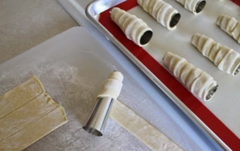 1. Этап. Трубочки с изюминкой: 5. Возьмите железные конусы или трубочки, оберните вокруг каждой (предварительно смажьте маслом) полоску слоеного теста, формируя трубочку.