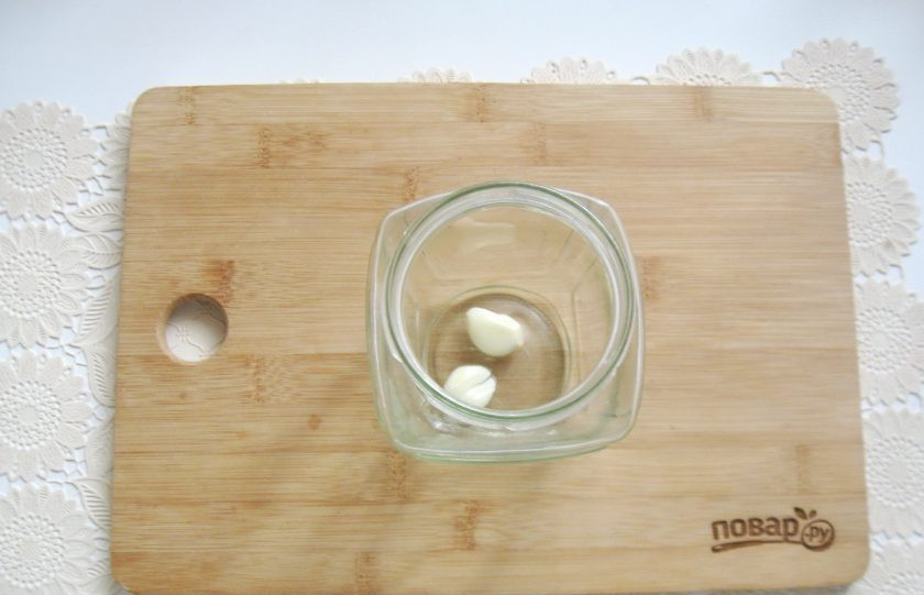 1. Этап. Маринованные шампиньоны на зиму: Банку простерилизуйте вместе с крышкой. На дно выложите зубчики чеснока.