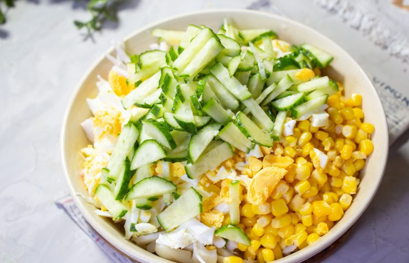 1. Этап. Салат с крабовыми палочками, кальмарами и кукурузой: Свежие огурцы помойте и обсушите, нарежьте тонкими брусочками и добавьте в салатник.