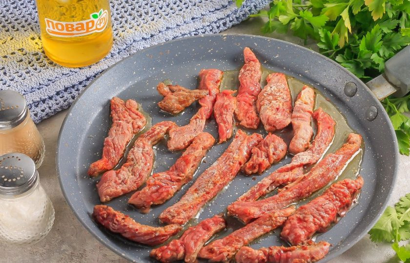 1. Этап. Соломка из говядины с репчатым луком: Разогрейте в сковороде растительное масло без аромата и выложите в него нарезку говядины. Обжарьте примерно 2-4 минуты с одной стороны. Время приготовления будет зависеть от толщины нарезки и степени нагрева. Нагрев должен быть средним, чтобы соломка не подгорела.