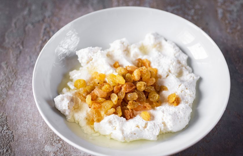 1. Этап. Вареники из рисовой муки: Приготовьте творожную начинку, для этого в тарелку выложите весь творог, добавьте яичный белок и изюм.