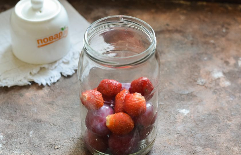 1. Этап. Компот из клубники и сливы на зиму: Банку для заготовки тщательно вымойте с пищевой содой, после ополосните хорошо под теплой проточной водой. Стерилизуйте банку удобным способом – над паром, в духовке или микроволновке. Крышку опустите в воду и проварите 10 минут. Переложите сливы и клубнику в банку.